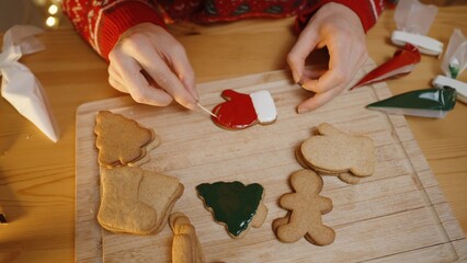 Hands Detail a Mitten-Shaped Cookie With Red and White Icing Using a Toothpick, While Various Plain and Decorated Cookies Rest on the Wooden Board.