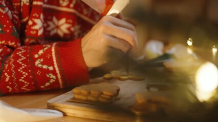 Woman in a Red Sweater Focuses on Decorating a Cookie With Red Icing, Surrounded by Other Cookies...