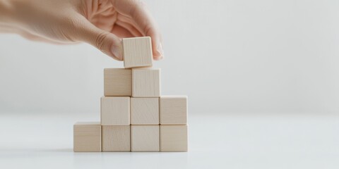 A hand carefully stacking wooden blocks in a creative arrangement on a clean, minimalist surface.