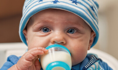 A baby in a striped hat drinks milk from a bottle