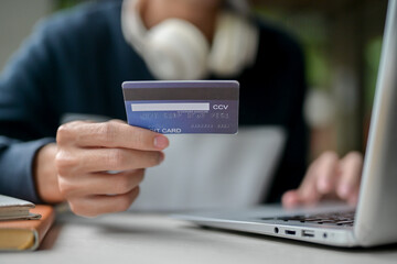 A close-up image of a man holding a credit card over a table while using his laptop.