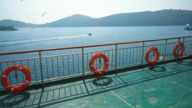  Sea of Marmara view from the ferry over the railing of a ship with attached orange lifebuoys. The hilly coast of Princes Islands on the horizon flying seagulls and passing motorboat