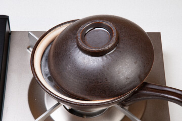 土鍋でお粥を作る。土鍋に米を入れて火にかける。沸騰したら弱火にし蓋をずらしてさらに煮る