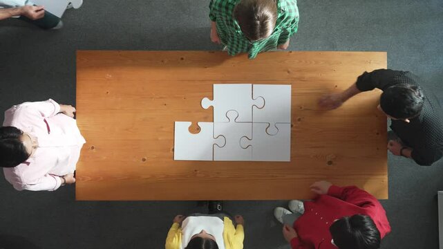 Top view of business man gathering last piece of jigsaw to complete puzzle. Group of diverse team working together to solve the puzzle while putting hands together and clapping hands. Convocation.