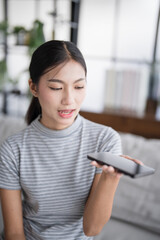 Asian woman using voice assistant on smartphone at home conversation with online assistant Voice chat bot conversational AI Modern Technologies.