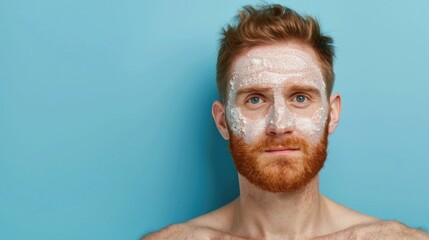 Closeup portrait of a handsome redheaded Caucasian man exfoliating and cleansing his skin with a gentle facial scrub against a vibrant blue background  The image showcases the man s thoughtful