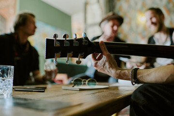 Selective focus closeup of hand of unrecognizable man sitting at coffee table playing guitar while...
