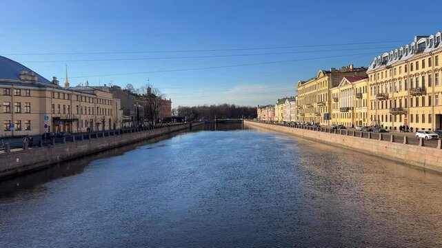 Russia, April 09, 2024: The Channel in St. Petersburg. Historical buildings on the river embankment, people walking along the embankment. Nevsky Canal in spring. Reflections of houses in the water. 4K