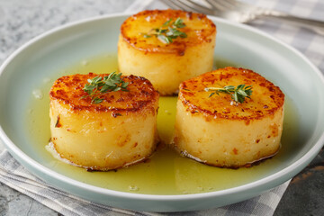 Melting potatoes braised with butter, stock, garlic, and fresh herbs, creating a spoonful of creamy flavors closeup on the plate on the table. Horizontal