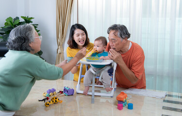 A little child eating his first meal, parents and grandparents cheer excitedly