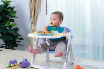 A little child eating his first meal on a high chair for children