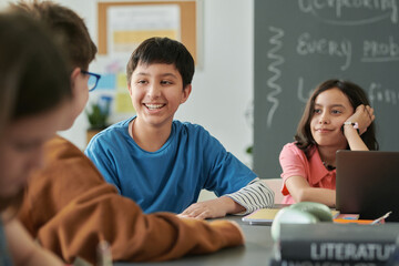 Portrait of smiling young boy talking to friends during class with group of kids in school copy space