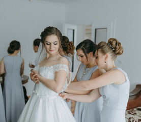 A bride is getting ready for her wedding with her bridesmaids. The bride is wearing a white dress...