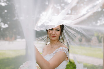 A bride is standing in front of a tree with a veil over her head. She is wearing a white dress and...