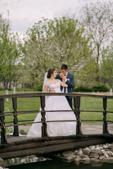 A bride and groom are standing on a bridge, with the bride holding a drink. Concept of love and happiness, as the couple is celebrating their wedding day