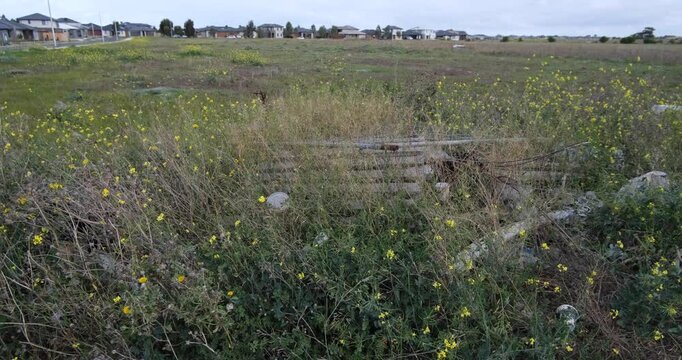 A vast, open field in Tarneit, Melbourne, awaits development in the residential suburb. The land is largely undeveloped, with some scattered litter and signs of illegal dumping on the ground.