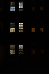 View of a dark building at night, with lights glowing through the windows, illuminating the facade against the dark surroundings © Em Neems Photography