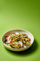 Salad with grilled zucchini, cherry tomatoes, and creamy goat cheese. presented on a white plate against a vibrant green background.