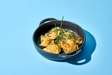 A close-up of a cast iron skillet filled with golden-brown, baked varenyky. The varenyky are garnished with fresh herbs on blue background.