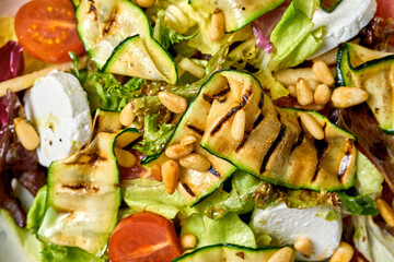 Salad with grilled zucchini, cherry tomatoes, and creamy goat cheese. presented on a white plate against a vibrant green background.