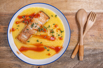 Bowl with polenta, grilled salmon, tomato sauce over wooden background.