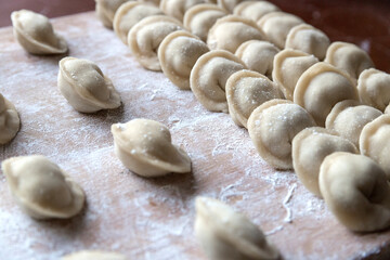 The raw dumplings were placed on a wooden cooking board, sprinkled with flour. The filling is minced meat, potatoes, cheese or cottage cheese. A semi-finished product, ready for cooking.
