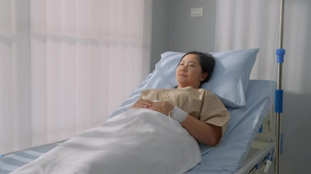 Asian mature female patient getting saline solution in hospital ward.