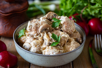 Hearty lunch: meatballs with mushrooms in cream sauce. Meatballs in a beautiful plate on a wooden table. Close-up