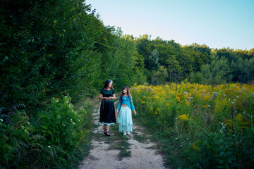 two woman in a whimsical aesthetic style dress in a field in the summer at sunset