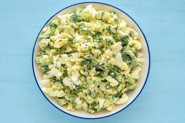 Egg Cucumber Thyme Salad in ceramic bowl over blue wooden background.