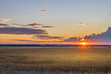 The sky radiates warm hues as the sun sets over a sprawling golden field, creating a tranquil...