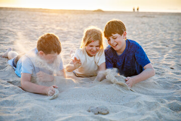 Three children playing with sand on sunset ocean beach. happy family, two school boys and one little preschool girl. Siblings having fun together. Bonding and family vacation in Andalucia, Spain