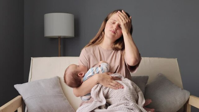 Mother embracing her baby girl while sitting on sofa tired concerned mother rocking sleeping baby in living room woman quietly lulling her child in her arms