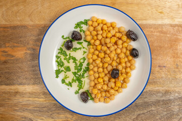 Chickpeas served with black olives, olive oil and chopped cilantro on ceramic plate.