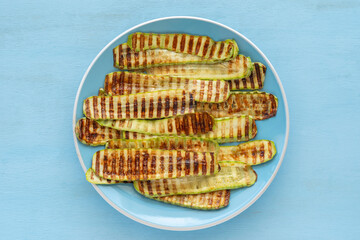 Grilled zucchini on blue ceramic plate over wooden background.