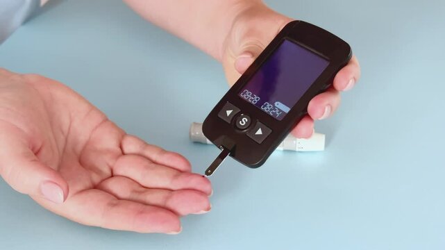 Diabetes monitoring concept. Woman using glucometer for checking blood sugar level. Blood sugar self control at home. Glucose test. Light blue background, 4k