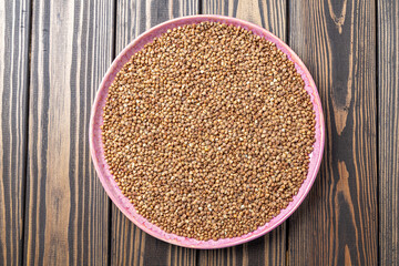 Buckwheat Grains on Plate on Wooden Background, Top View, Copy Space.Hulled kernels of buckwheat grains close up. Food background.