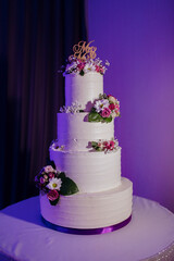 A four tier wedding cake with a purple ribbon and a gold lettering that says Merry