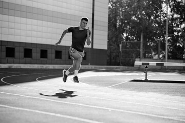 Black and white photo. Focused runner sprints around track, his determined expression matching peed of his stride. Concept of sport, tournament, motivation, workout, competition. Ad