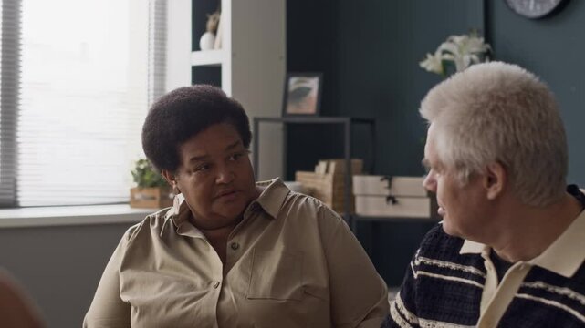 Waist up of multiracial old couple going through marriage breakdown sitting by their family psychologist at modern office and having argument