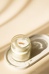 Handmade candle from paraffin and soy wax in glass with wooden wick isolated on pastel beige background. Flat lay, top view, copy space