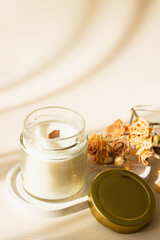 Handmade candle from paraffin and soy wax in glass with wooden wick and dry herbal isolated on pastel beige background. Flat lay, top view, copy space