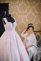A woman is sitting in front of a wedding dress. The dress is white and has lace detailing. The...