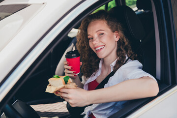 Photo of cheerful pretty lady dressed white shirt drinking coffee driving rented automobile eating...