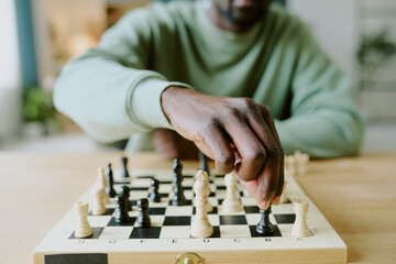 Closeup of hand of unrecognizable African American chess player moving pawn while solving problem