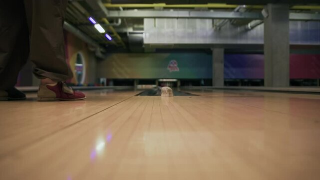 Low section of two unrecognizable people wearing bowling shoes throwing bowling balls on lanes towards pins while playing together indoors