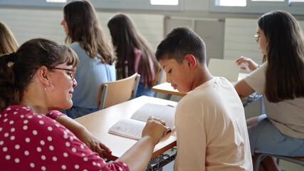 Young Teacher helping hispanic student boy to understand homework exercise at primary school classroom - Powered by Adobe