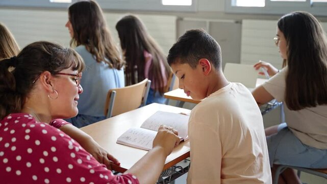 Young Teacher helping hispanic student boy to understand homework exercise at primary school classroom - Powered by Adobe