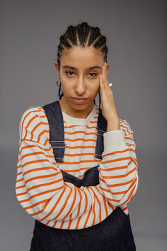 Vertical waist up portrait of smug young woman with cornrows hairstyle posing confidently on grey background in studio and looking at camera