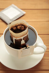 Drip coffee bag with ground coffee in cup on brown wooden background. Vertical photo
